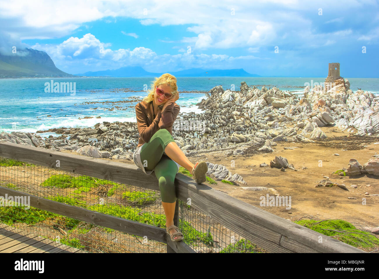 Donna felice ad elevata visualizzazione boardwalk della colonia di pinguini nel punto pietroso riserva naturale vicino alla città costiera di Betty's Bay, Western Cape, Sud Africa. Turista femminile godendo con i Penguins africani. Foto Stock