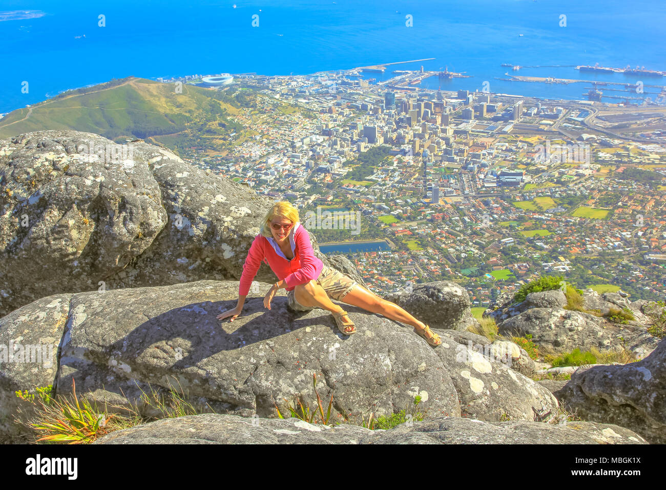 Viaggiatore caucasica seduta dopo un trekking in montagna della tavola NP. Sportivo da donna gode di vedute panoramiche del porto di Città del Capo e il mare dalla cima del monte Table, Western Cape, Sud Africa. Foto Stock