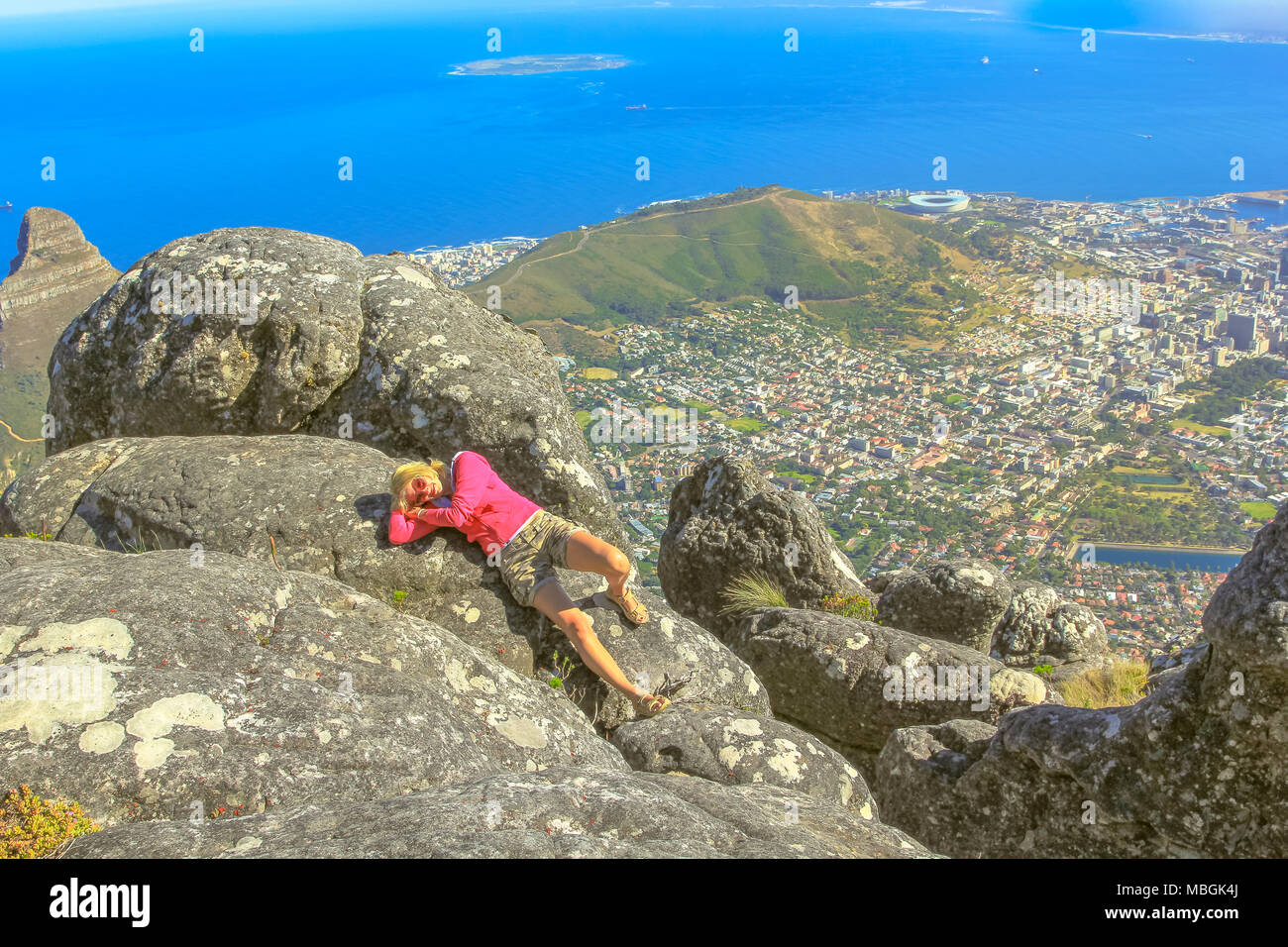 Giovane viaggiatore disteso dopo un trekking in montagna della tavola NP. Sportivo da donna gode di vedute panoramiche del porto di Città del Capo e il mare dalla cima del monte Table, Western Cape, Sud Africa. Foto Stock