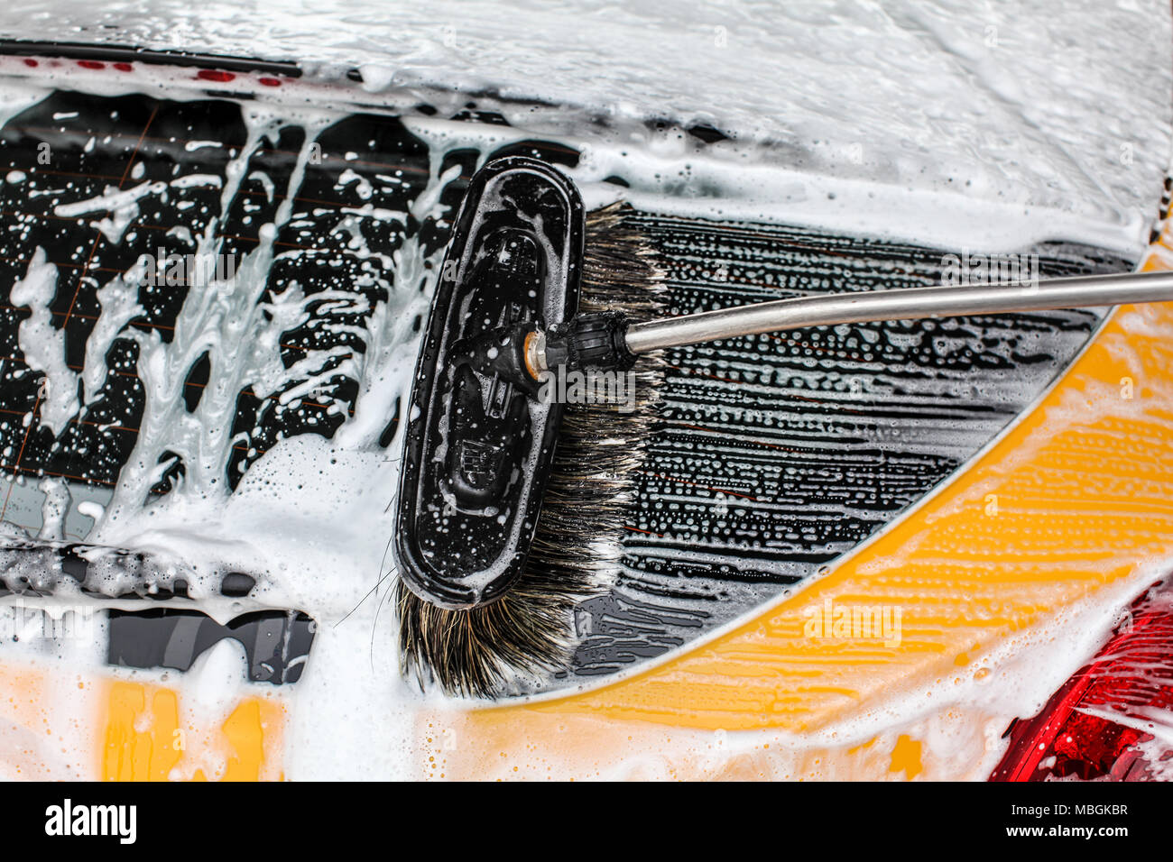 Dettaglio di colore giallo scuro auto finestra posteriore lavato in autolavaggi. Spazzola corse di lasciare in bianco il sapone e lo shampoo schiuma. Foto Stock