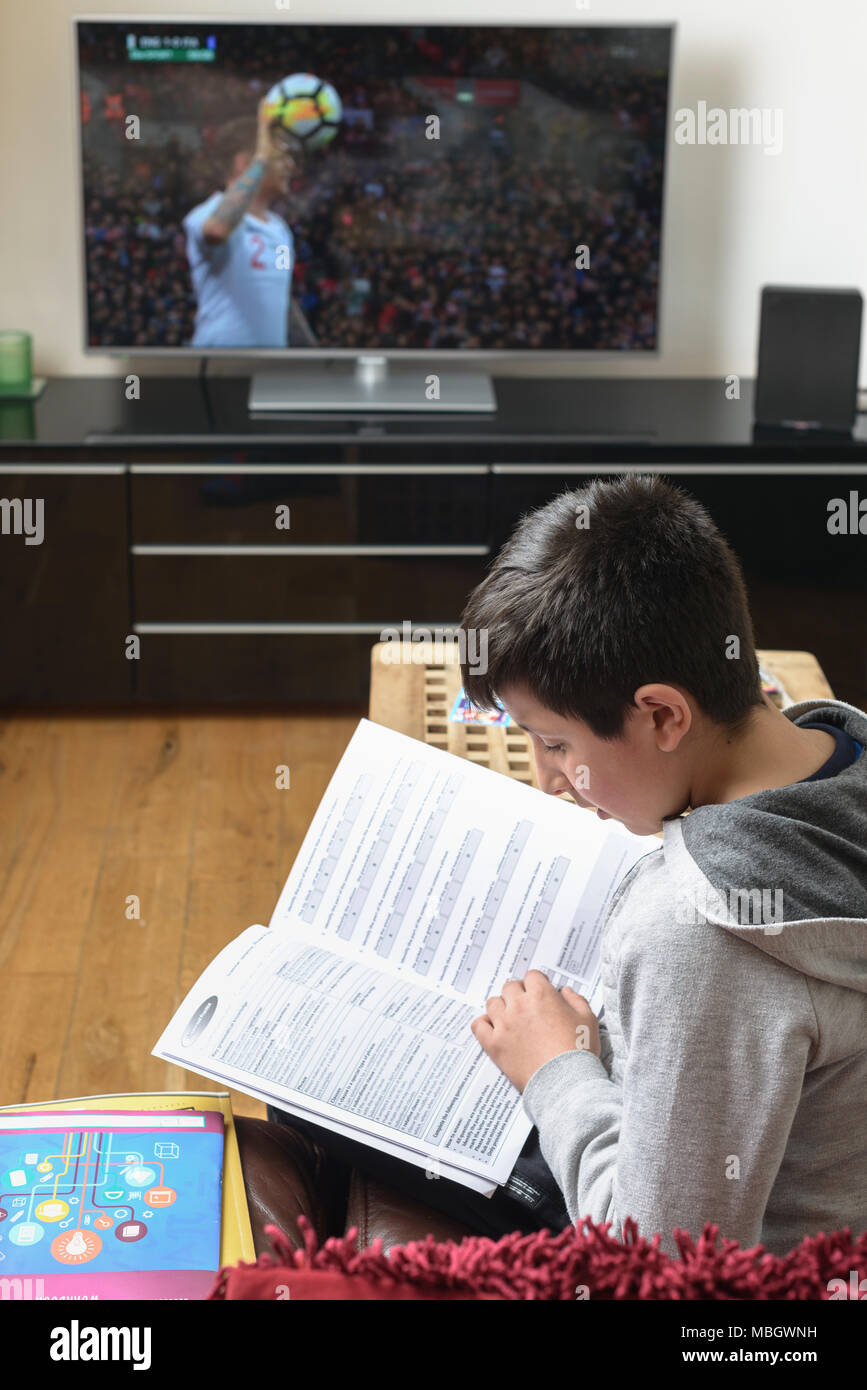 UK-Schoolboy ,10 anni ,cercando di studio durante la partita di calcio viene riprodotto sulla TV Foto Stock