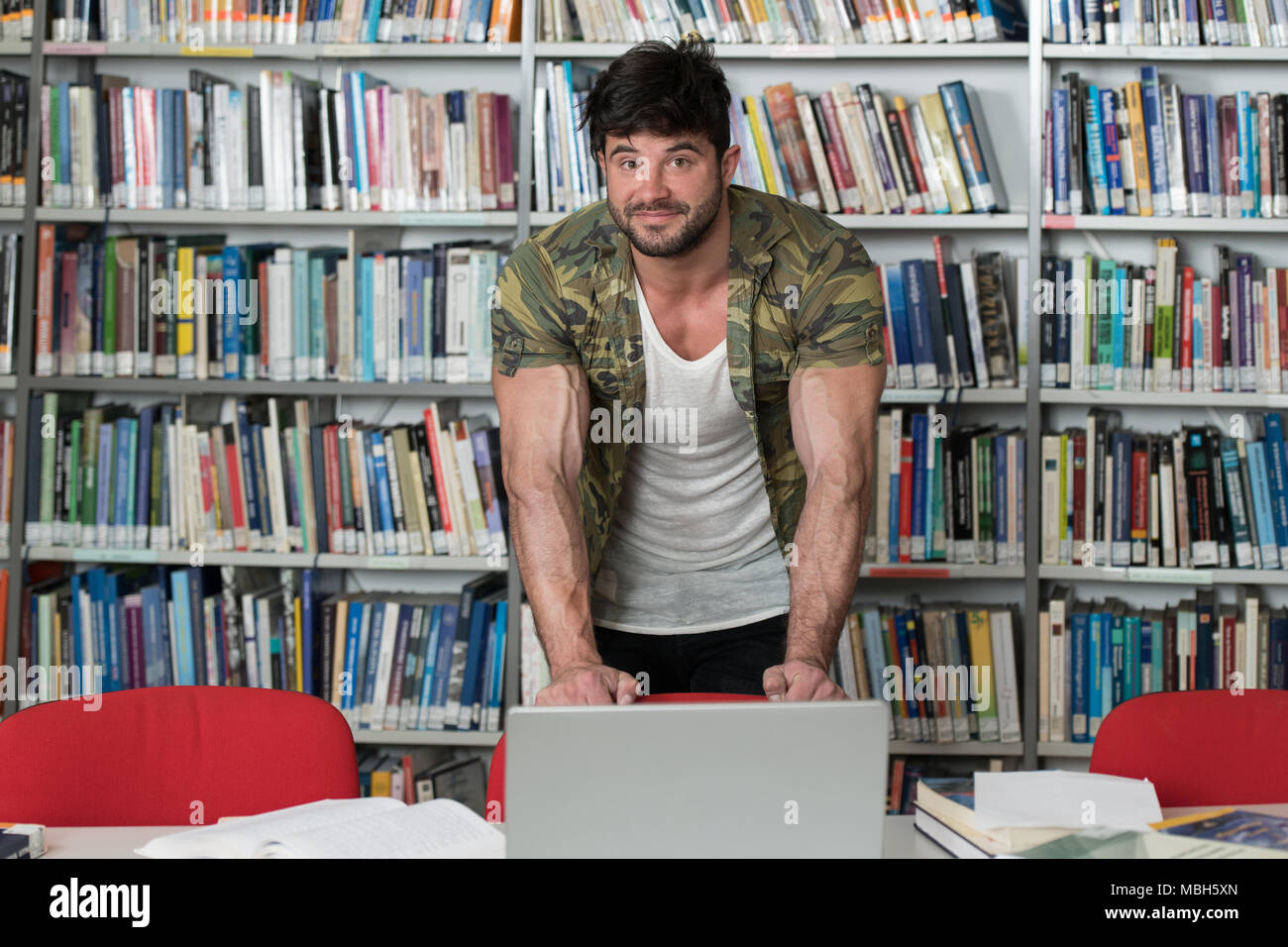 Bel uomo muscoloso con i capelli scuri in piedi la biblioteca - Bodybuilder Preparazione Esame e lezioni di apprendimento nella biblioteca della scuola Foto Stock