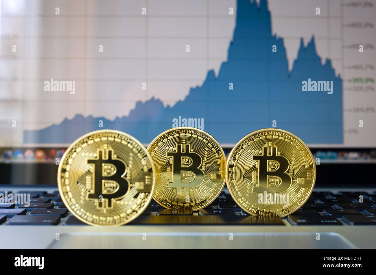 Tre bitcoins su un computer portatile con la tendenza dei prezzi graffic sullo sfondo Foto Stock
