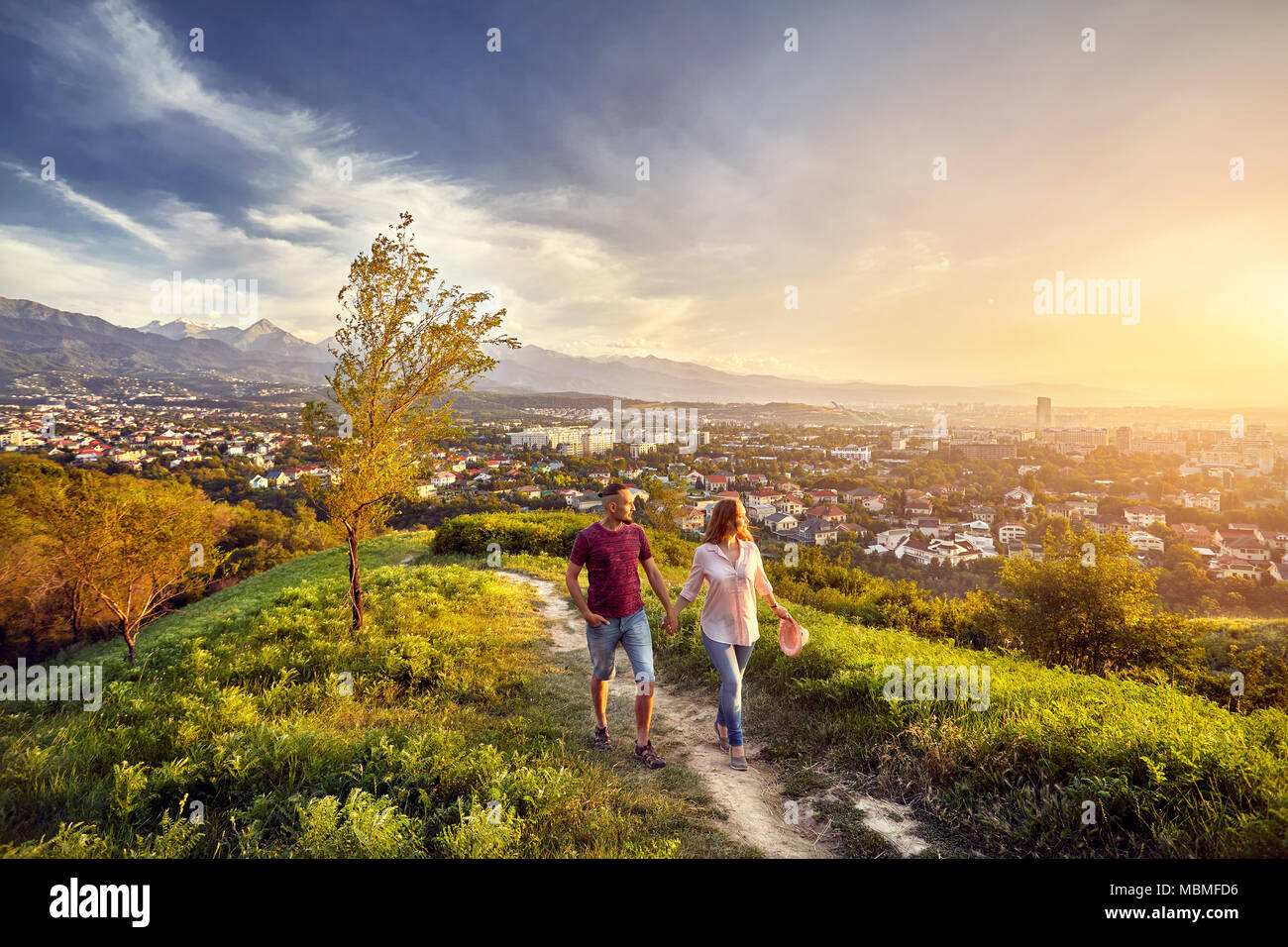 Yong giovane in abiti rosa passeggiate nel parco al tramonto vista città sullo sfondo. Foto Stock