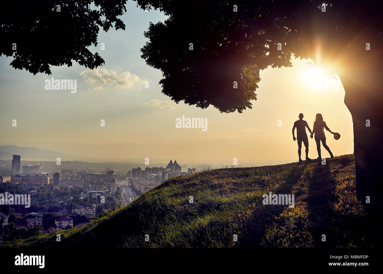 Yong matura in silhouette tenendo premuto dalle mani e guardando il tramonto panorama della città Foto Stock