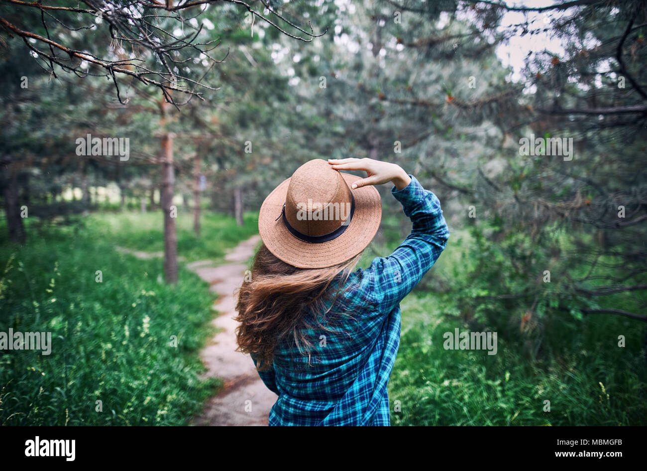 Giovane donna in marrone cappello e verde maglietta controllati con capelli lunghi in piedi sul disco vento sotto alberi di pino della foresta Foto Stock