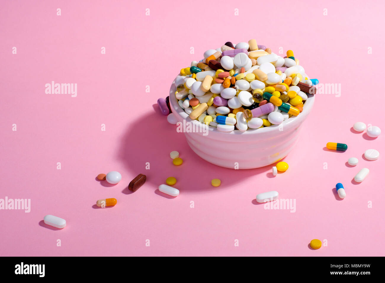 Ciotola piena di pillole colorate su sfondo rosa. Composizione creativa. Foto Stock