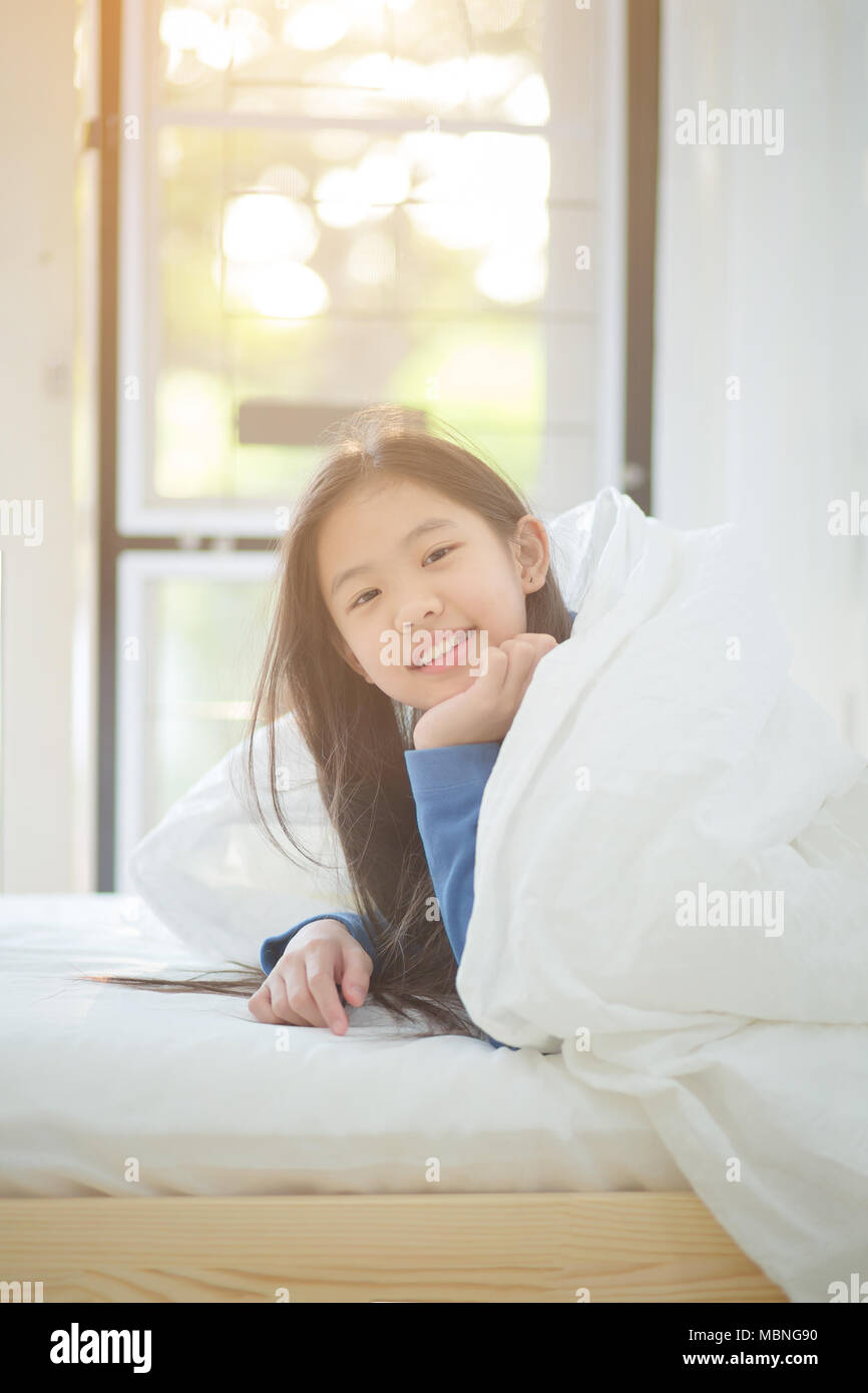 Felice ragazza asiatica sdraiato sul letto con la luce del sole sul giorno pigro Foto Stock
