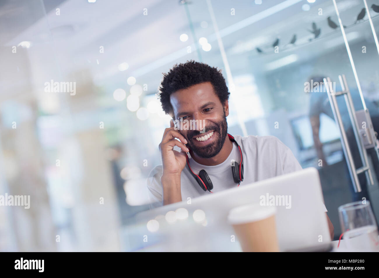 Sorridente e fiducioso imprenditore creativo parlando su smart phone al computer portatile in ufficio Foto Stock