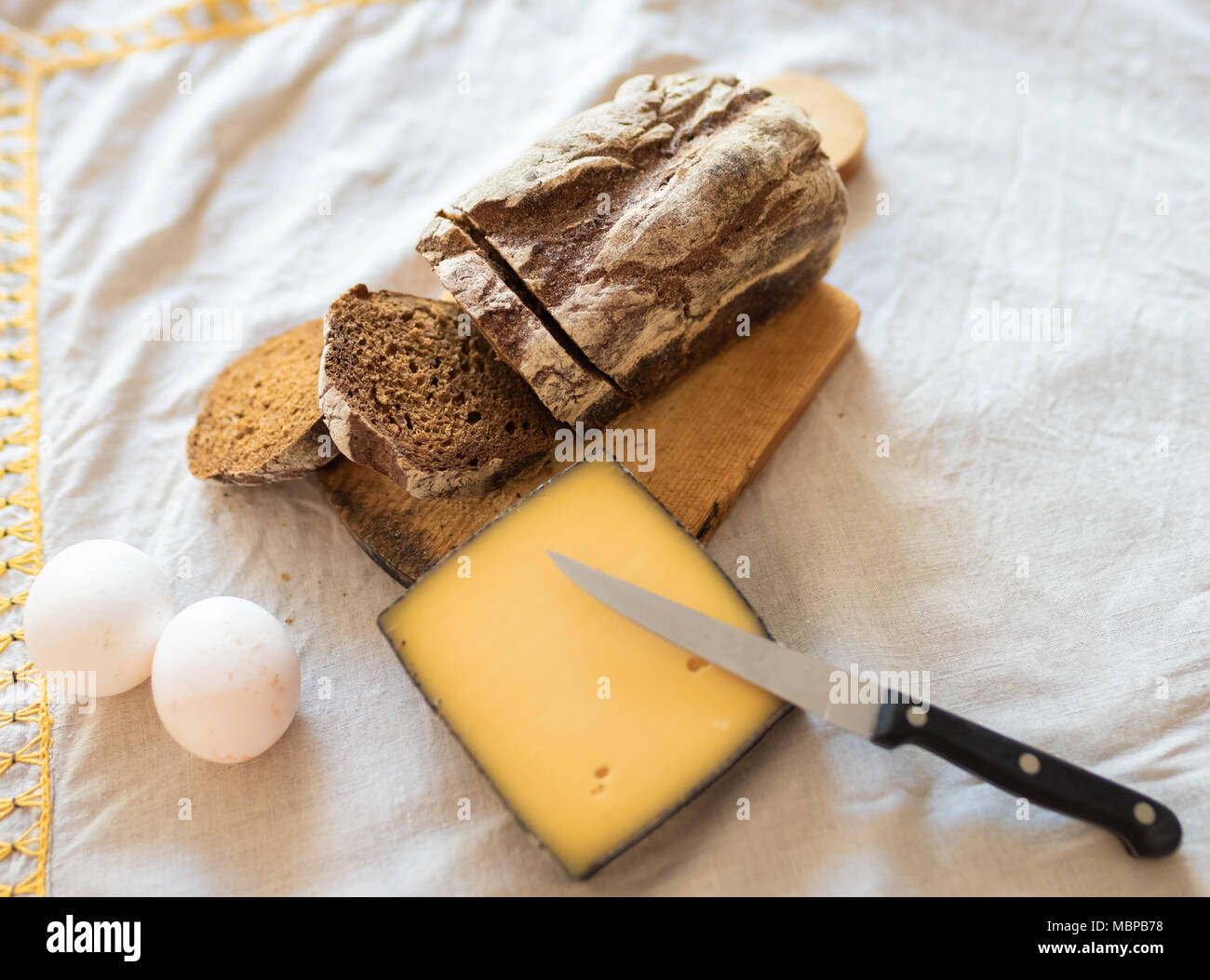 Una fetta di formaggio, due uova e una pagnotta di pane su un tavolo con una tovaglia di lino. Vista dall'alto. Foto Stock