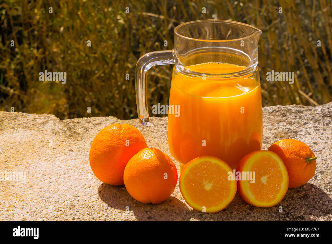 Succo d'arancia appena spremuto in una caraffa di vetro, preparata con arance fresche, all'esterno con sfondo naturale Foto Stock