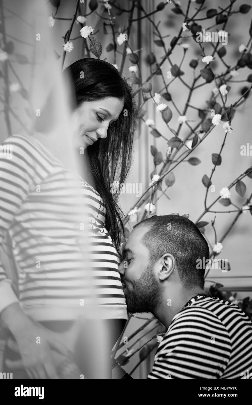Foto in bianco e nero di attraente coppia internazionale in striped maglioni guardare a ogni altro uomo musulmano si sedette e bacia la pancia del suo preg Foto Stock
