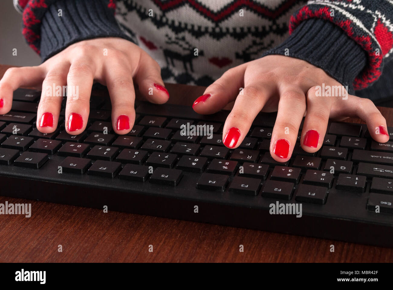 Femmina in maglione digitando sulla tastiera del computer con le mani e unghie rosse polacco. Close up Foto Stock