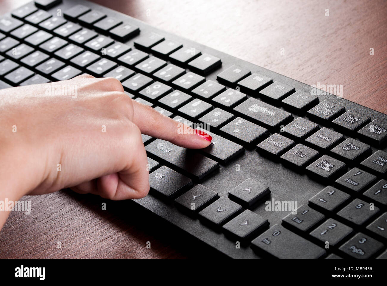Ragazza dito premere il tasto Invio sulla tastiera del computer sulla scrivania in legno. Close up Foto Stock