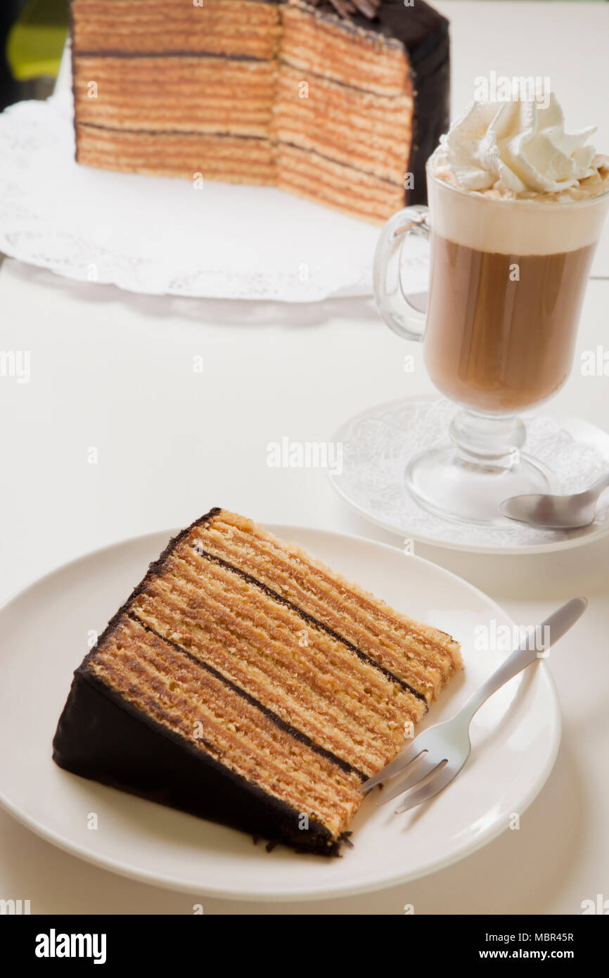 Fetta di torta dello strato sulla piastra con forcella e cappuccino e caffè Foto Stock