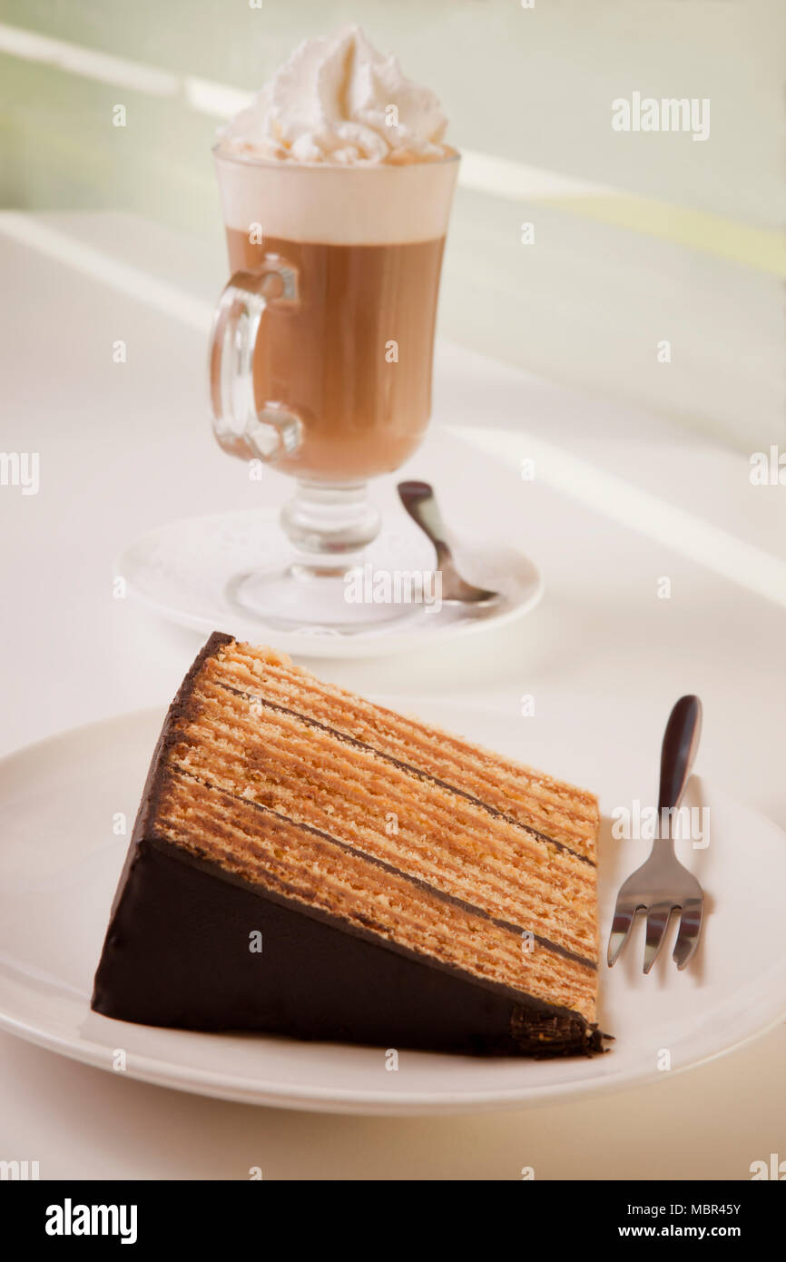 Fetta di torta dello strato sulla piastra con forcella e cappuccino e caffè Foto Stock