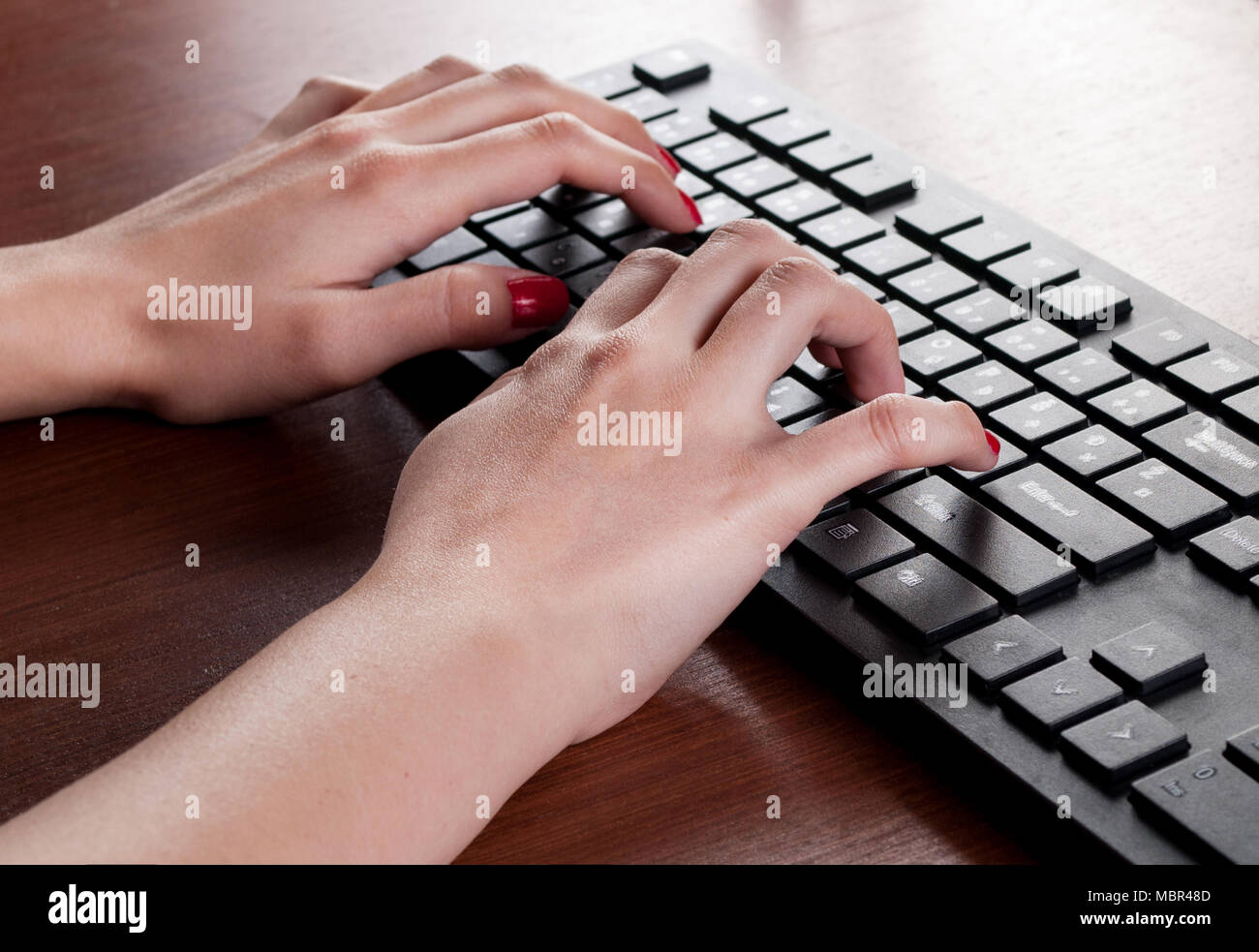 Giovane femmina la digitazione su nero della tastiera del computer sulla scrivania di legno in ufficio. Close up Foto Stock