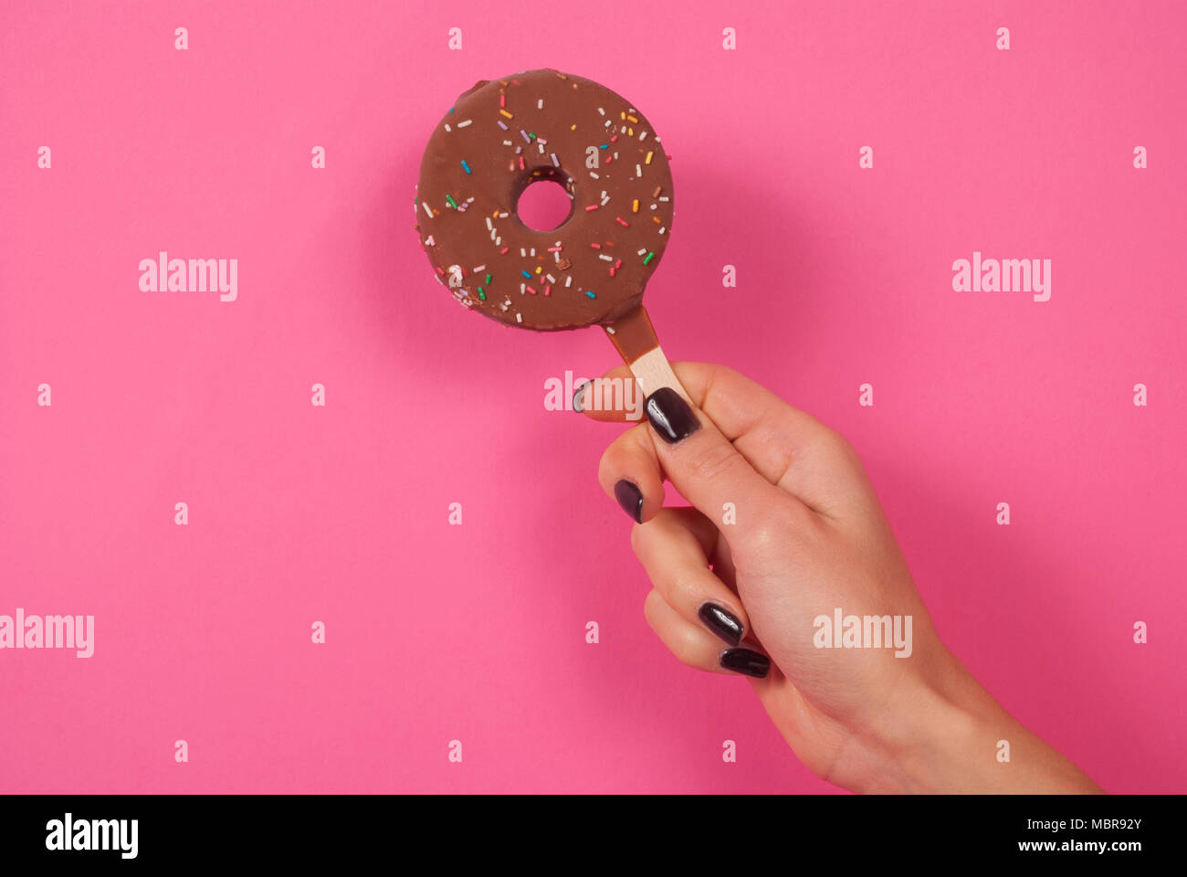 Ragazza con donut gelati su un bastone su sfondo rosa, close up Foto Stock