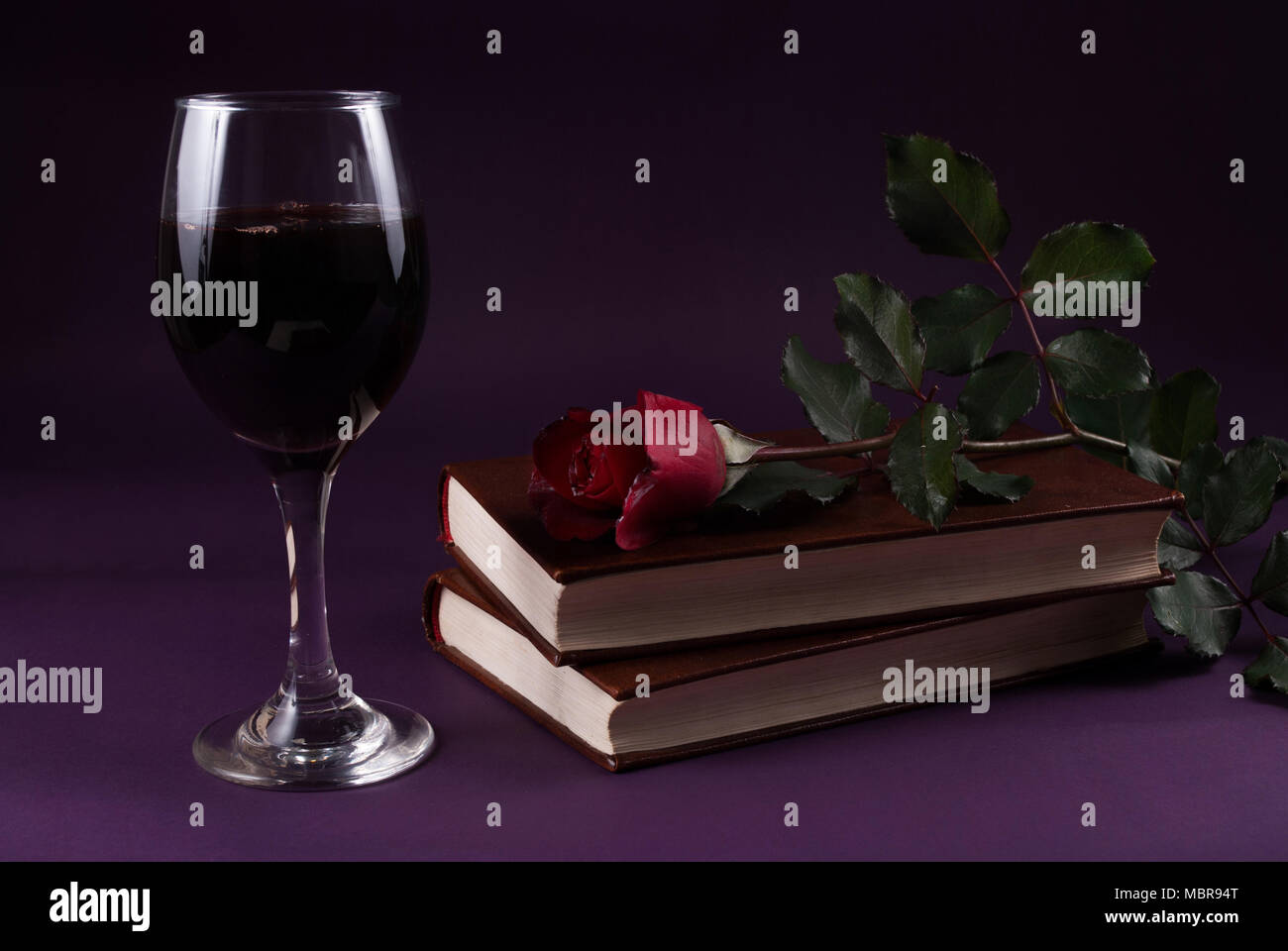 Red Rose fiore su libri e bicchiere di vino sul viola scuro dello sfondo,  Halloween concetto chiave di basso Foto stock - Alamy