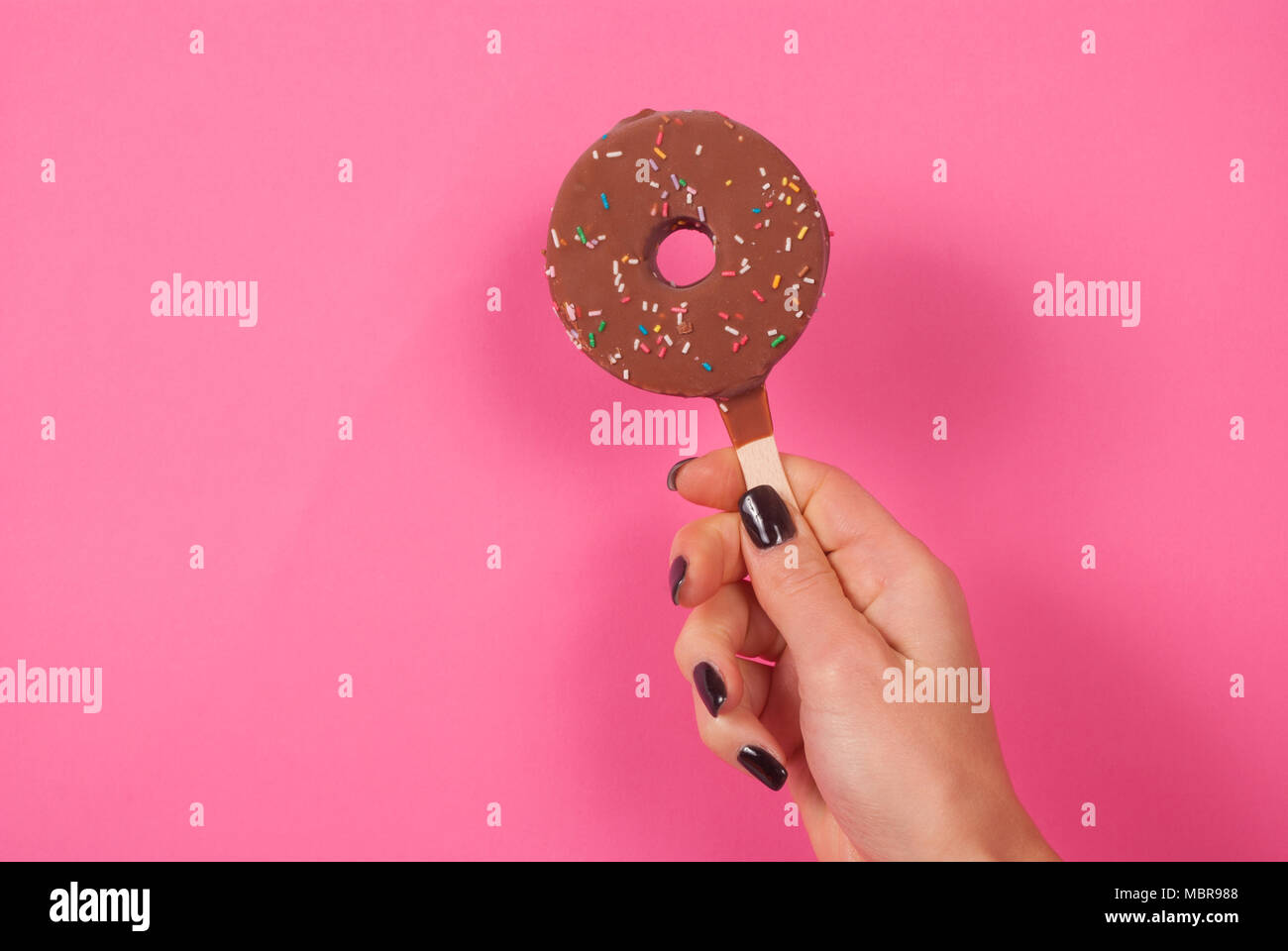 Ragazza giovane con mano a ciambella gelati su un bastone su sfondo rosa Foto Stock