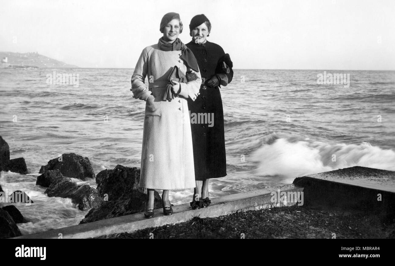 Moda, due donne in cappotti e con il cappello e borsetta in posa sulla costa, 1920s, Italia Foto Stock