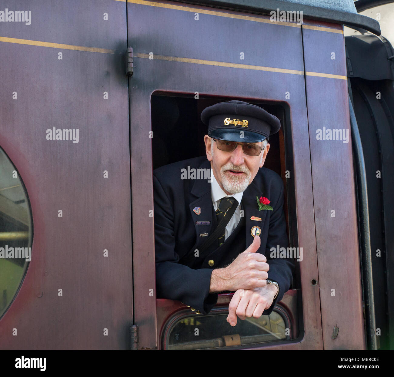 Chiusura del Caucaso in treno senior di guardia, in berretto, isolato sporgersi di vintage carrozza ferroviaria finestra dando una felice "Thumbs up'. Foto Stock