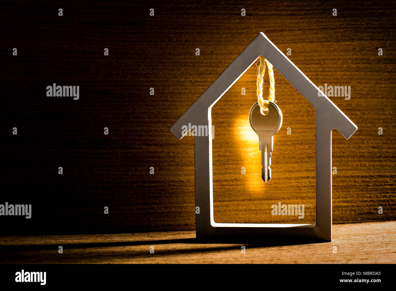 Chiave di Argento appeso all'interno di casa bianca su vintage sfondo di legno con la riflessione della luce. Concetto per immobili, mobile home o locazione. Foto Stock
