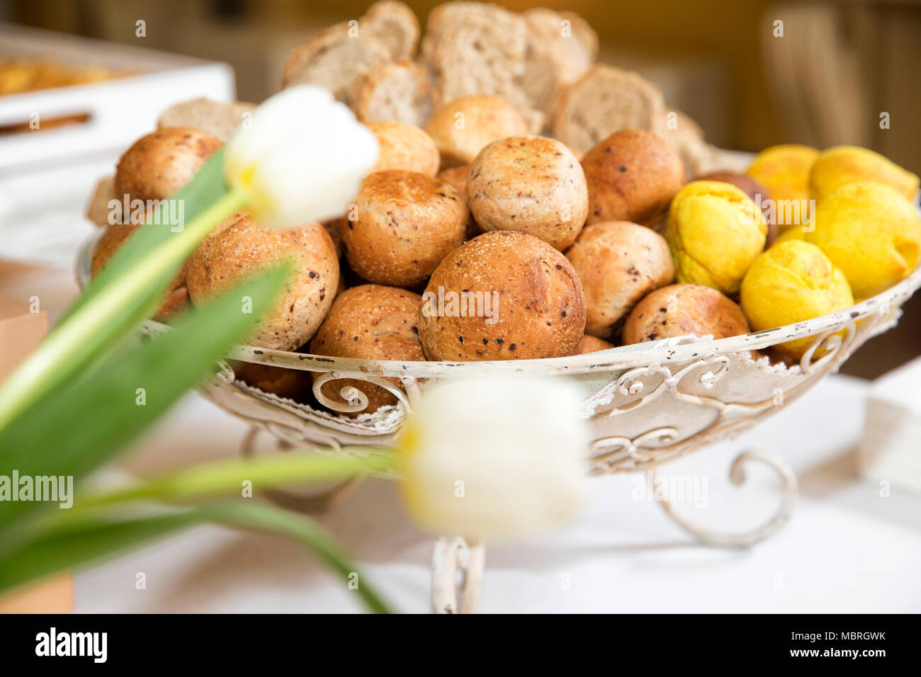 Primo piano di un buffet di nozze, frumento integrale poco pane in un metallo vintage riser con fuori fuoco tulipani bianco sulla destra Foto Stock