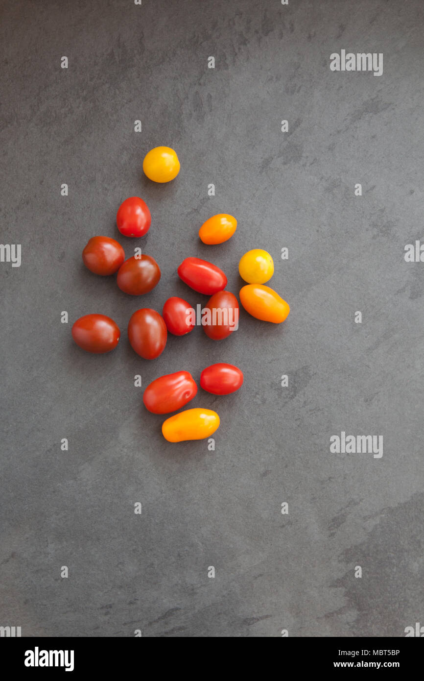 Materie prime: la ciliegia e la prugna baby i pomodori in una varietà di colori mostrata disteso su una scheda di ardesia Foto Stock