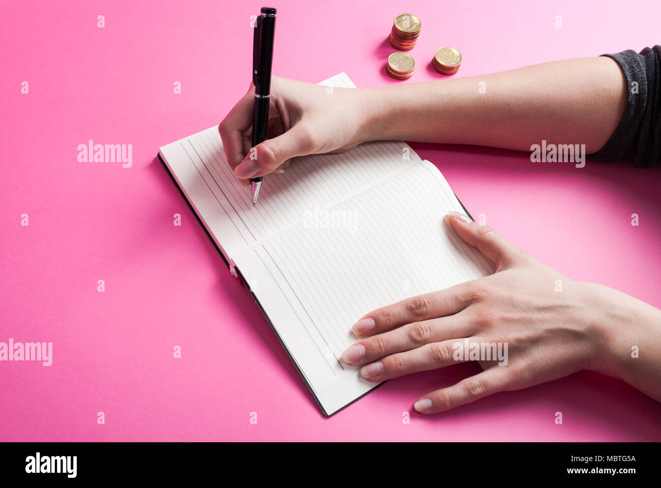 Scrive a mano nel notebook e moneta metallica su sfondo rosa Foto Stock