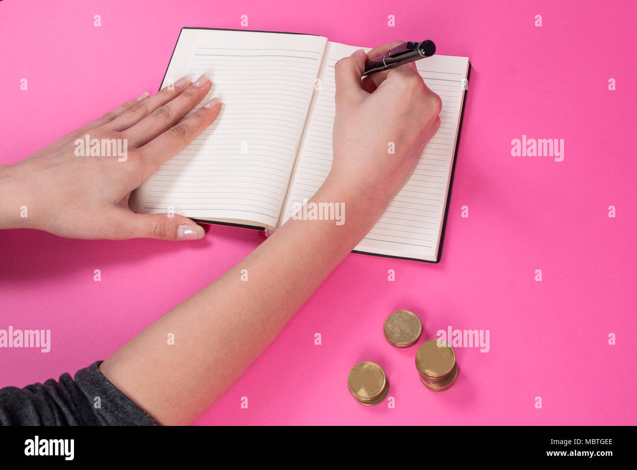 Donna mano trattiene una penna in mano e ha scritto accanto alla moneta sullo sfondo rosa Foto Stock