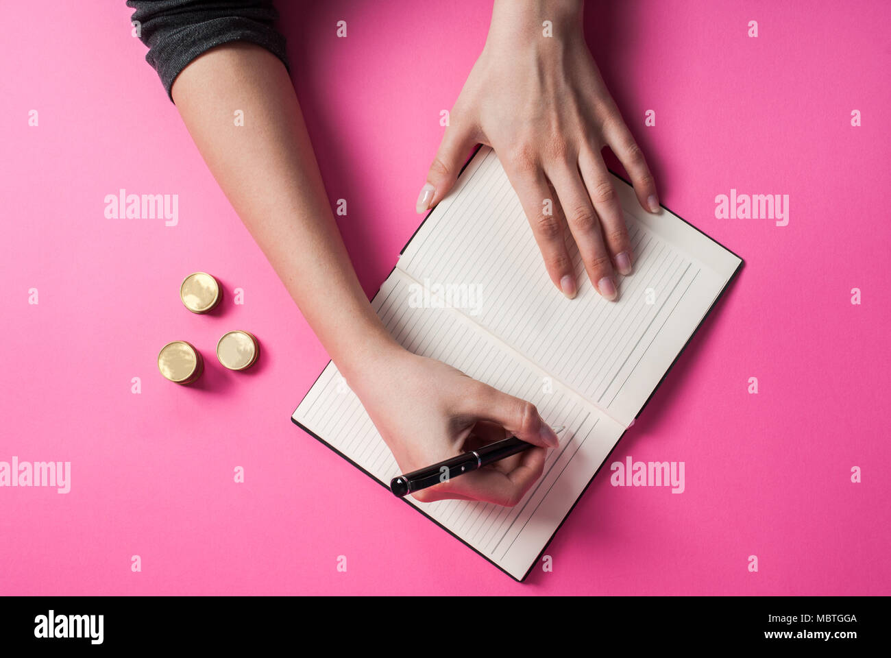 La donna la scrittura a mano con una penna in un notebook e moneta sullo sfondo rosa Foto Stock