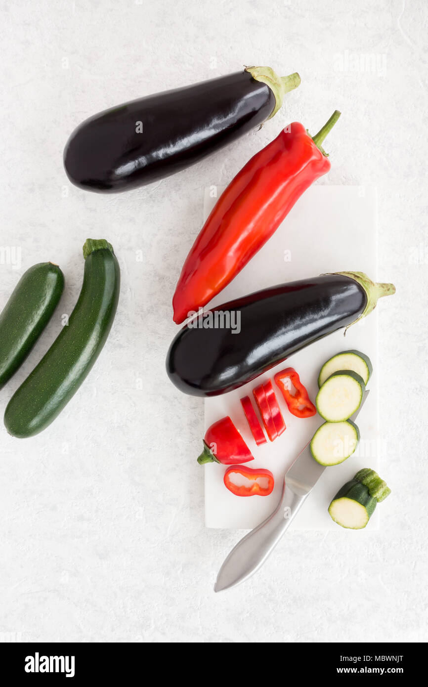 Vista dall'alto di melanzane, appuntita dolci peperoni e zucchine su un marmo bianco tagliere. Foto Stock