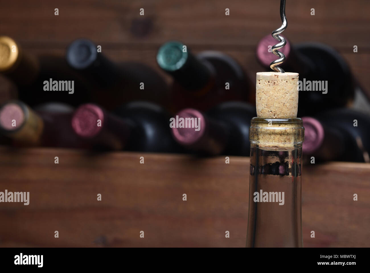 : Closeup di una bottiglia di vino con il tappo di sughero parzialmente estratto. Un fuori fuoco case di legno di vino è in background. Foto Stock