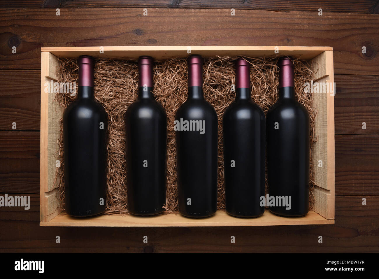 Caso di vino rosso: vista dall'alto di una scatola di legno di bottiglie di vino rosso al buio su un tavolo di legno, il caso viene riempito con paglia di imballaggio. Foto Stock