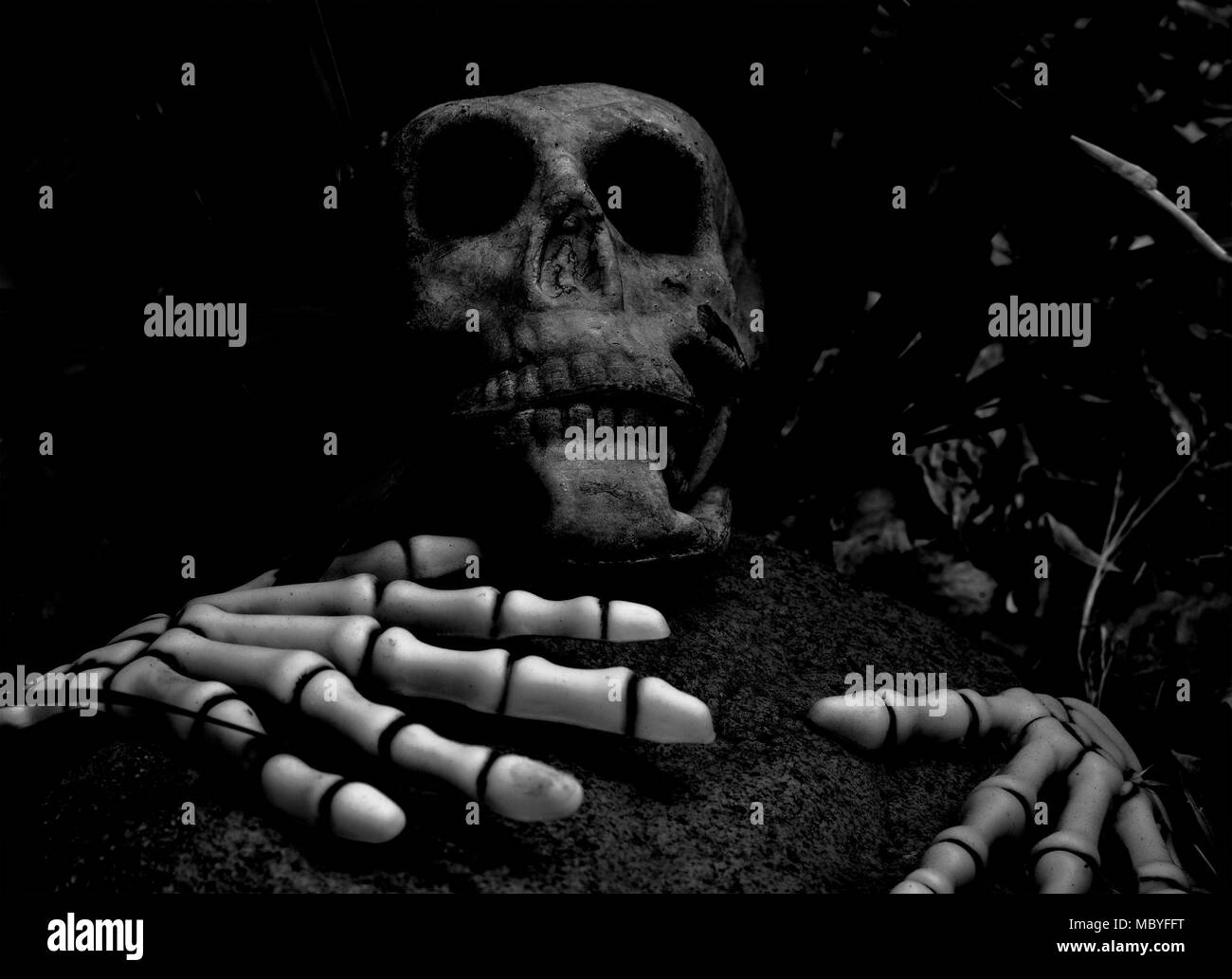 Un teschio e lo scheletro di mani suggerendo una persona è stata uccisa da un big rock- spooky halloween decorazione in bianco e nero Foto Stock