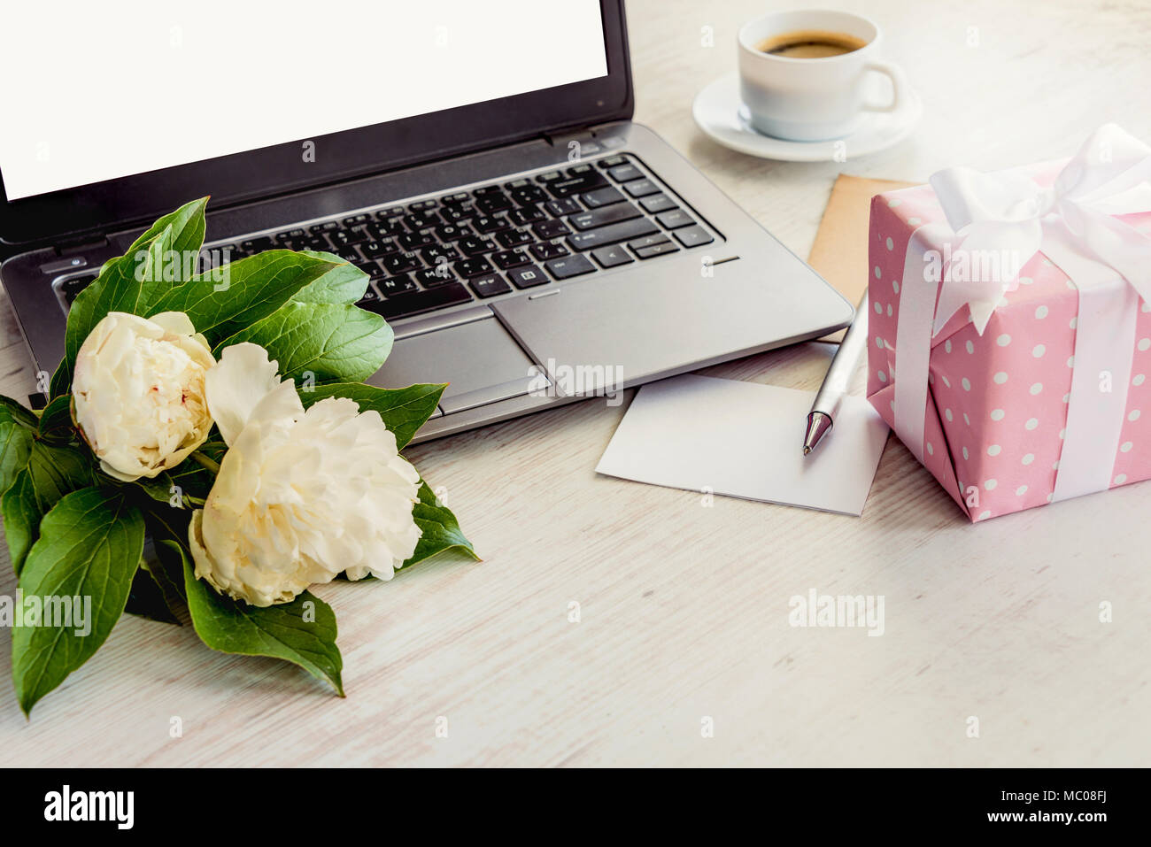 Vista laterale di un mazzo di carte con computer, bouquet di fiori di peonie, tazza di caffè, scheda vuota e rosa punteggiato confezione regalo. Bianco in legno rustico sfondo. Rom Foto Stock