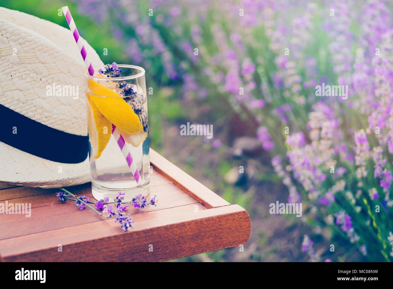 Un bicchiere di limonata fresca e un cappello di paglia su una sedia in legno. Fioritura di fiori di lavanda in background. Foto Stock