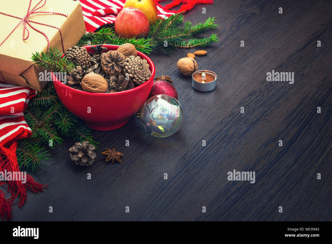Decorazione di natale - rosso ciotola piena di abeti-coni, confezione regalo avvolti in carta kraft, rami di pino, candela, dadi, anice, mele, giocattoli di Natale e rosso Foto Stock