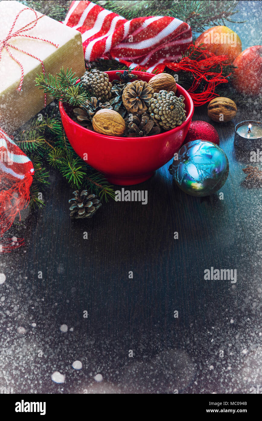 Decorazione di natale - rosso ciotola piena di abeti-coni, confezione regalo avvolti in carta kraft, rami di pino, candela, dadi, anice, mele, giocattoli di Natale e rosso Foto Stock
