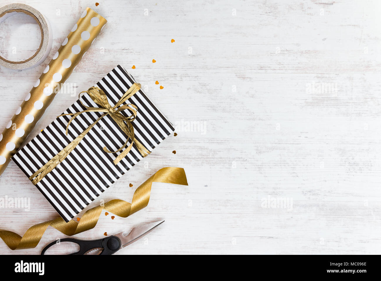 Confezione regalo avvolto in bianco e nero a strisce di carta con golden bow e i materiali di confezionamento su un legno bianco sfondo vecchio. Spazio vuoto. Foto Stock