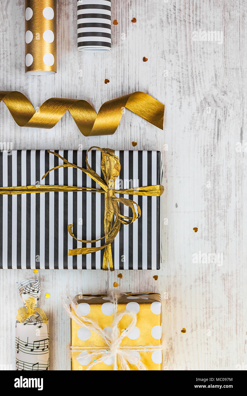 Confezioni regalo avvolto in bianco e nero a strisce e golden punteggiato di carta e materiali di imballaggio su di un legno bianco sfondo vecchio. Foto Stock