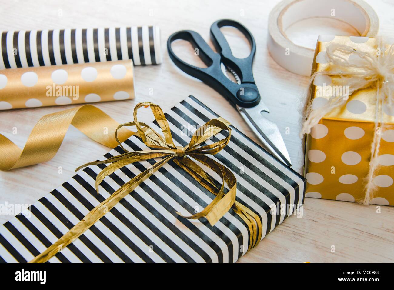 Close up di confezioni regalo avvolto in bianco e nero a strisce e golden punteggiato di carta e materiali di imballaggio su di un legno bianco sfondo vecchio. Foto Stock
