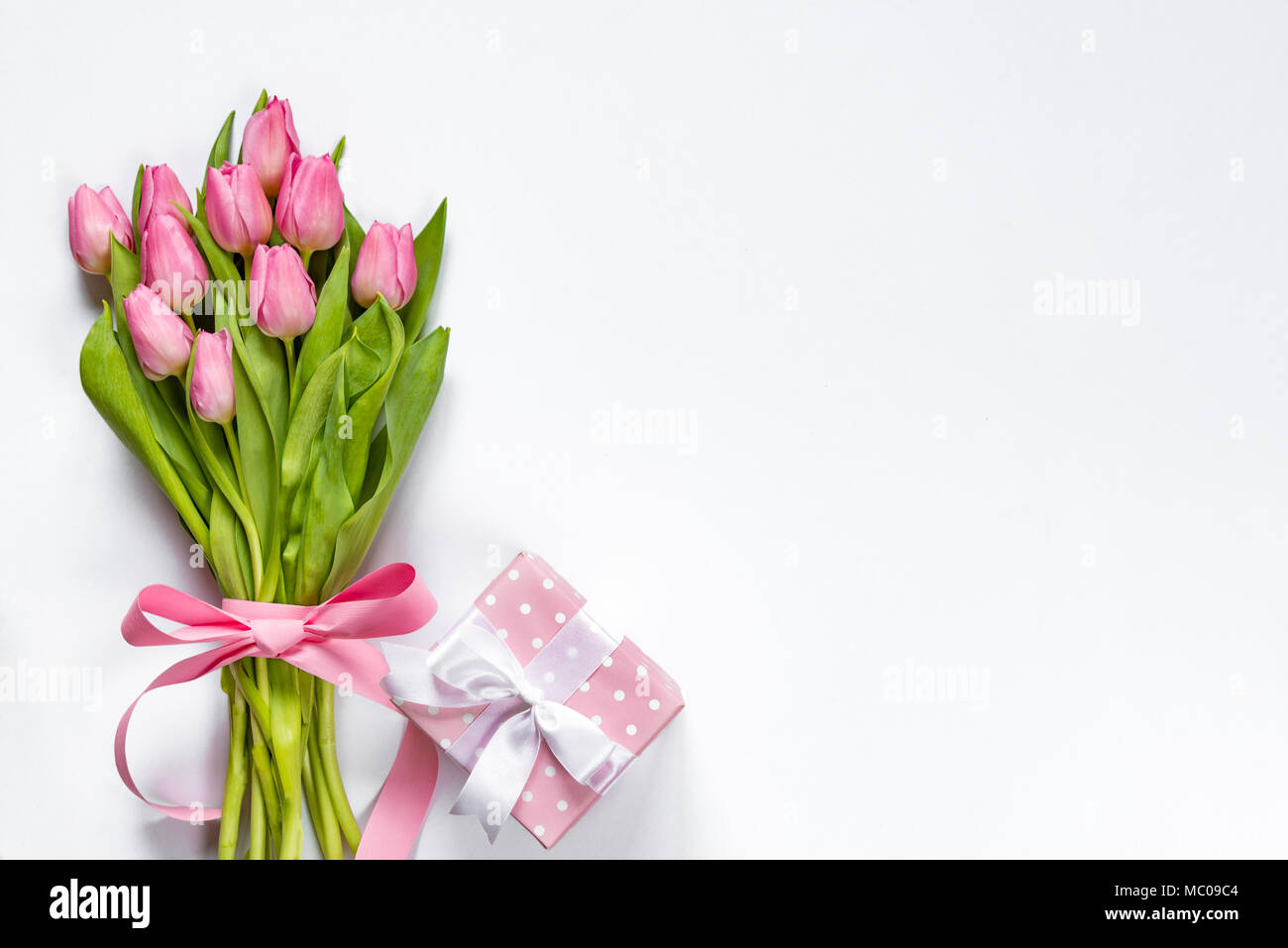 Vista superiore della rosa bouquet di tulipani, avvolti con il nastro rosa e rosa punteggiato confezione regalo su sfondo bianco. Copia dello spazio. Foto Stock