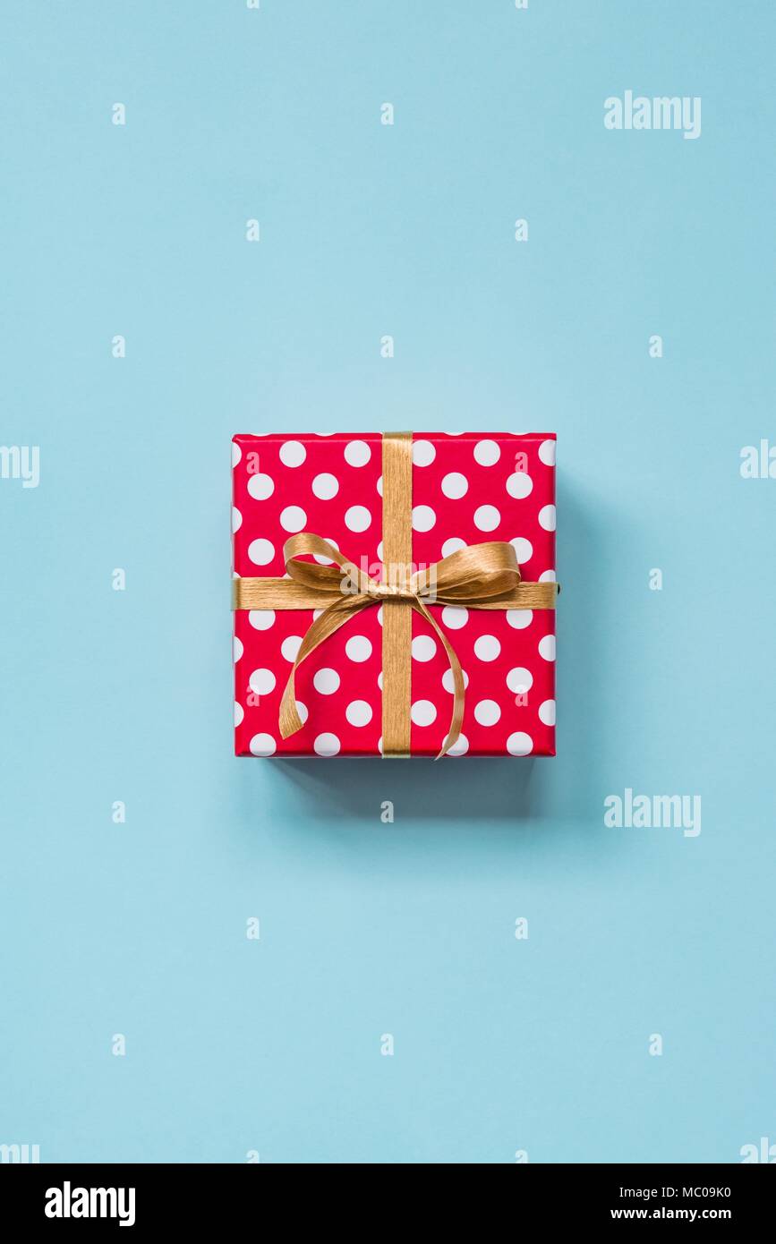 Vista dall'alto di una rossa tratteggiata scatola regalo legato con la golden bow su sfondo blu. Foto Stock