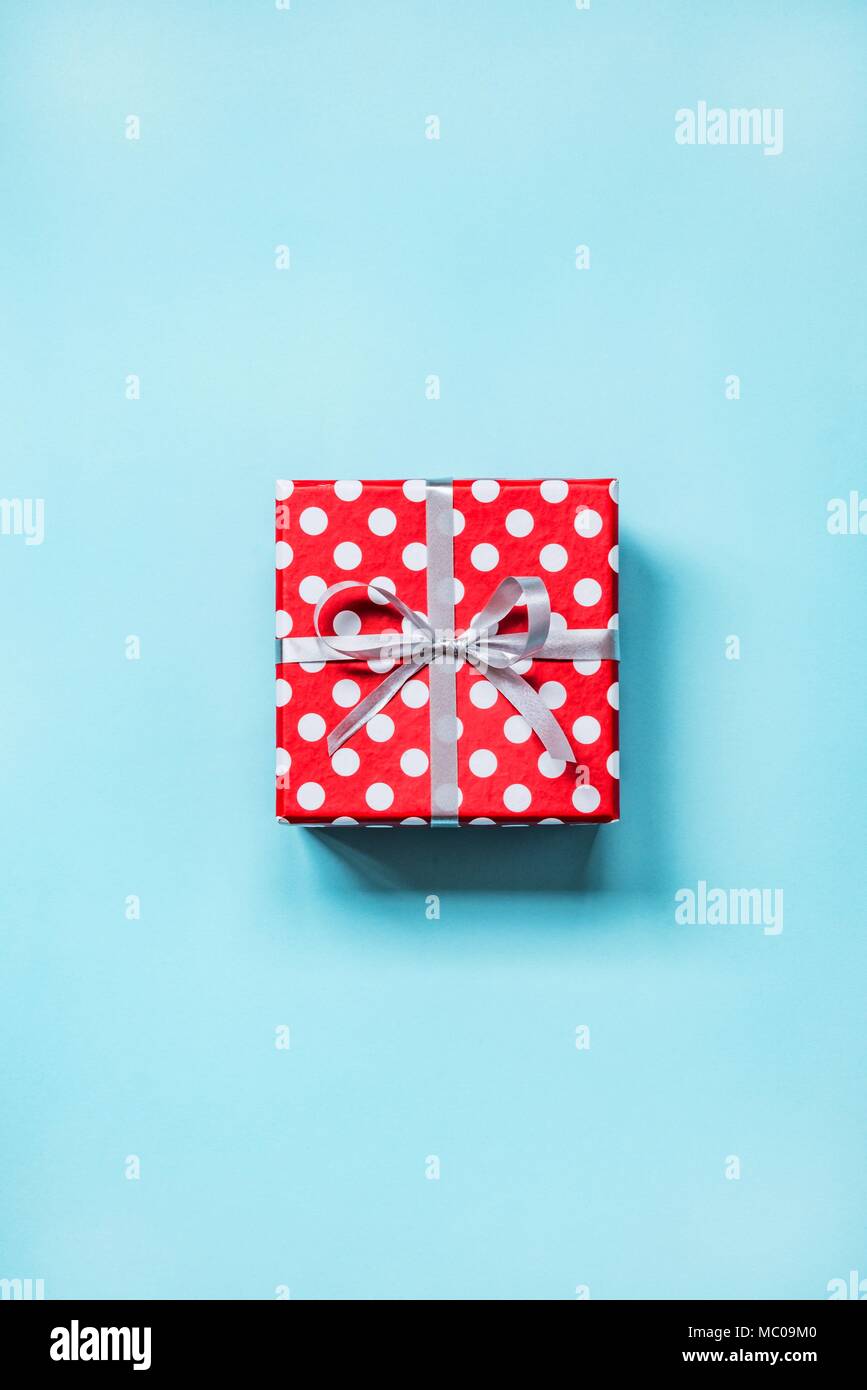 Vista dall'alto di una rossa tratteggiata scatola regalo legato con la golden bow su sfondo blu. Foto Stock
