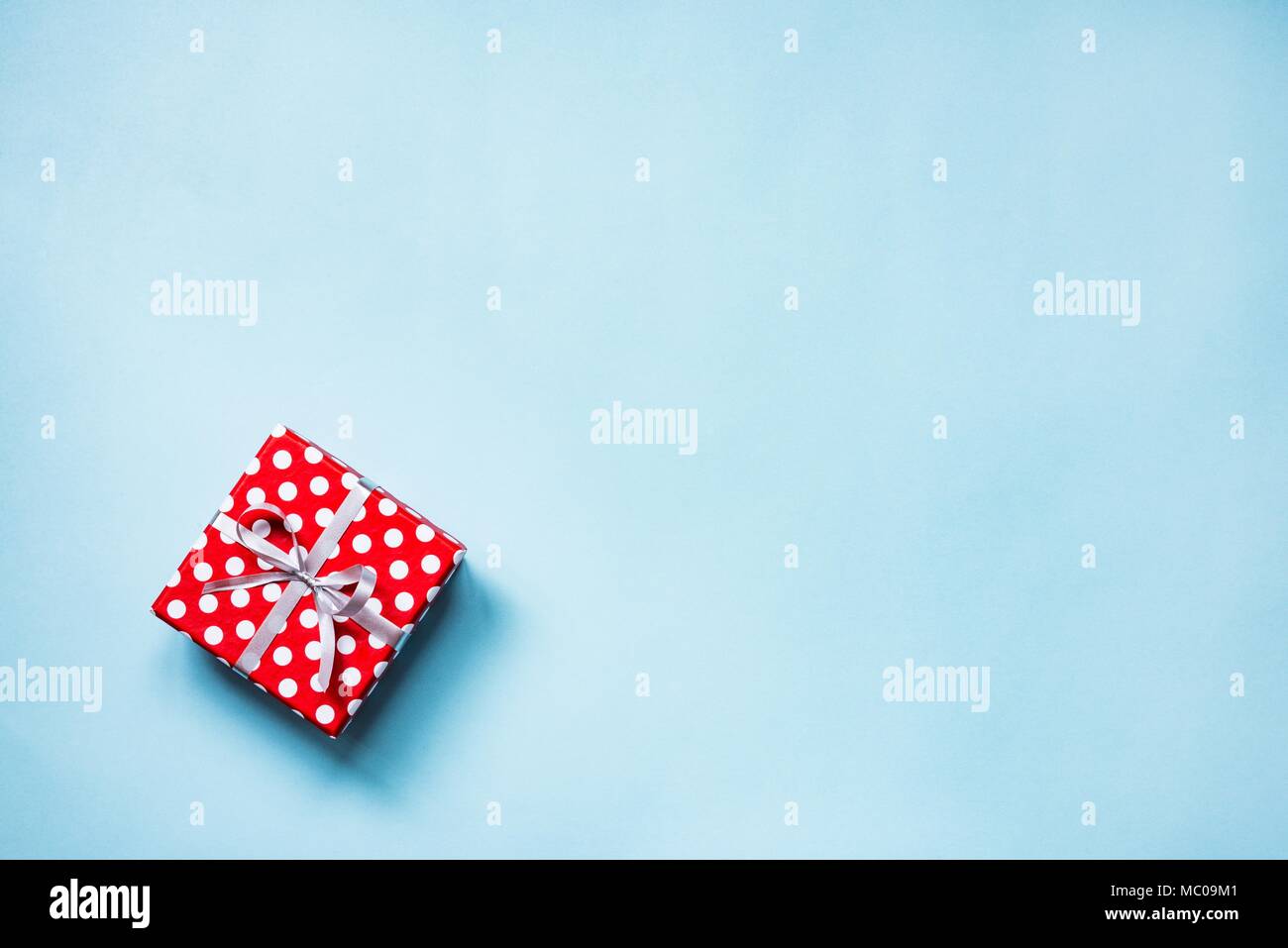 Vista dall'alto di una rossa tratteggiata scatola regalo legato con la golden bow su sfondo blu. Copia dello spazio. Foto Stock