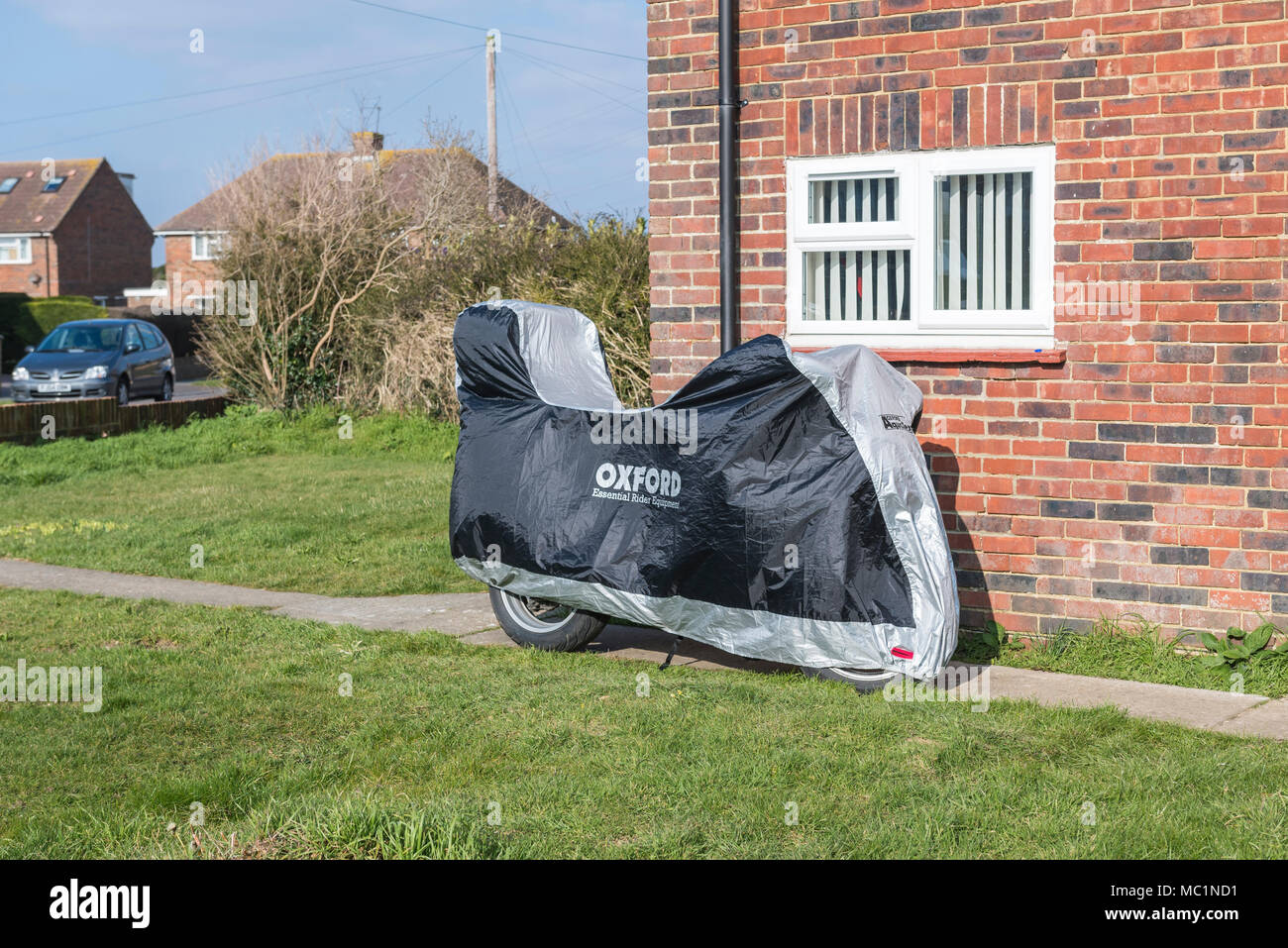 Un motociclo parcheggiato al di fuori di una casa con una copertura di protezione su di esso. Coperto per moto. Foto Stock
