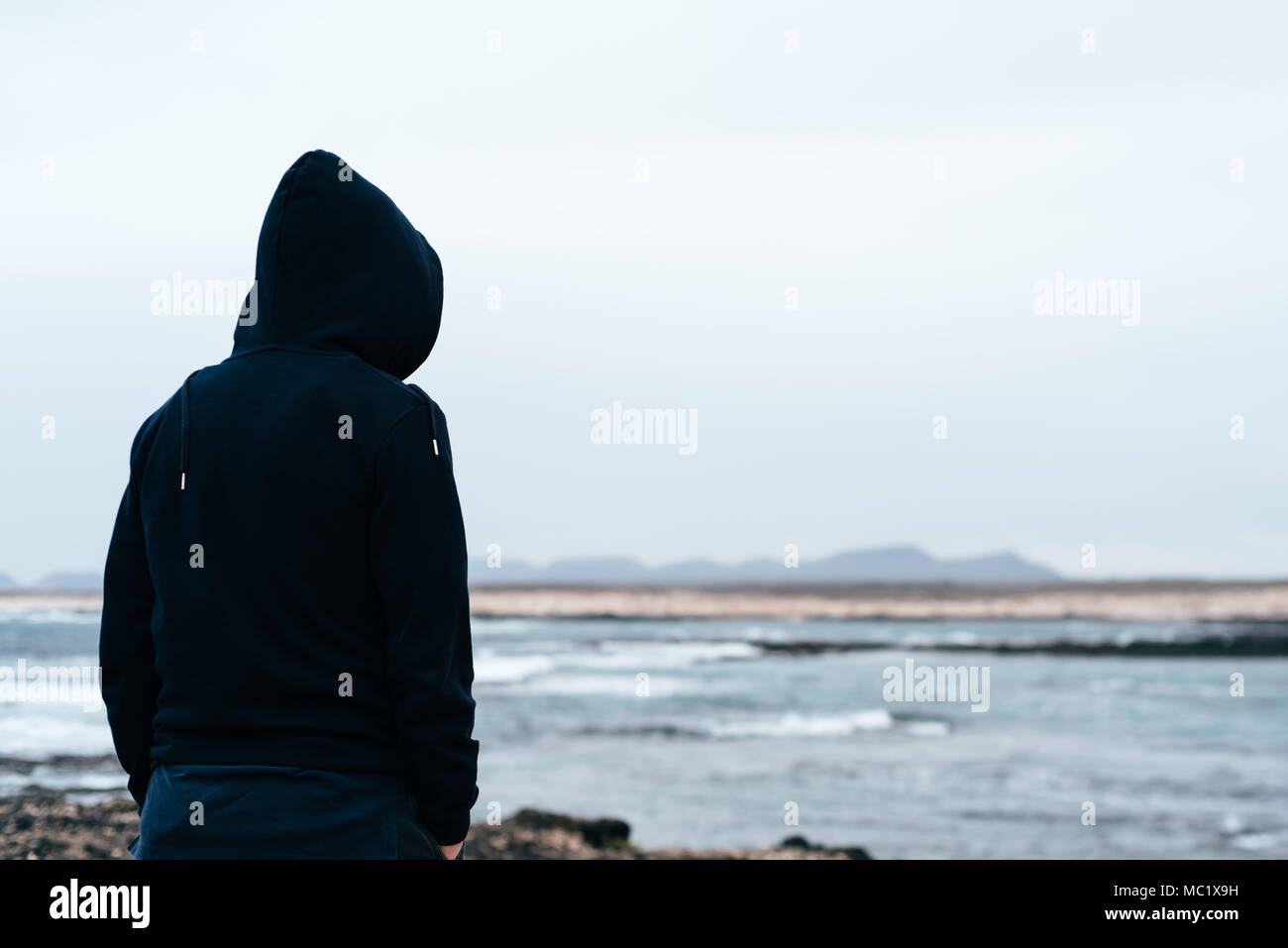 Uomo che indossa hoodie guardando il mare. Vista posteriore del concetto di solitudine Foto Stock
