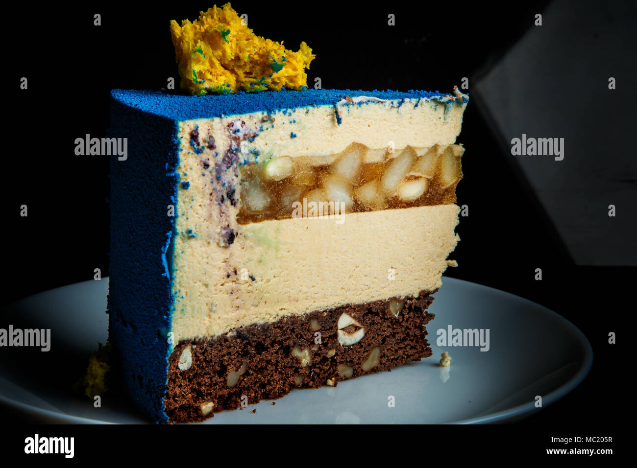 Closeup pezzo di mousse di blu la torta con la spugna gialla decorazione torta sulla parte superiore e caramello pera strato inter sorge sulla piastra